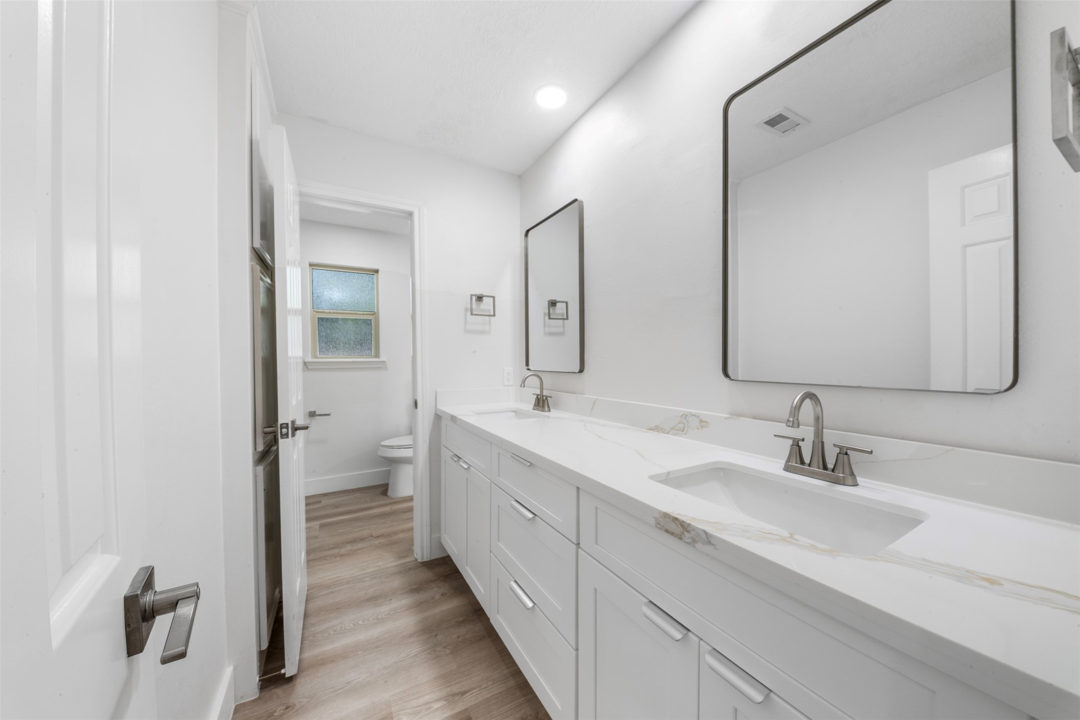 9543 Enstone Circle Spring, TX 77379 - Photo 28 of 50 This bathroom features a modern double vanity with sleek faucets and large mirrors, bright white cabinetry for ample storage, and a separate area for the toilet. The light wood flooring and recessed lighting create a clean, spacious feel.