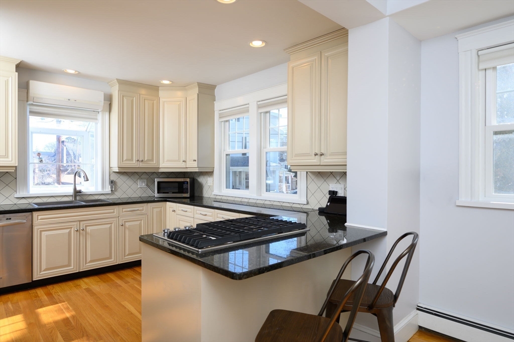 1099 Brook Road Milton, MA 02186 - Photo 13 of 41 a kitchen with granite countertop a stove a sink and white cabinets