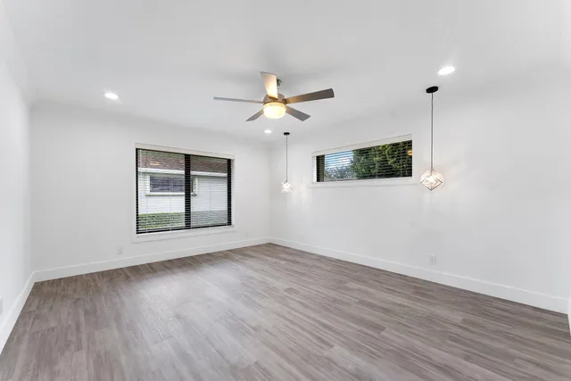 a view of an empty room with wooden floor and a ceiling fan