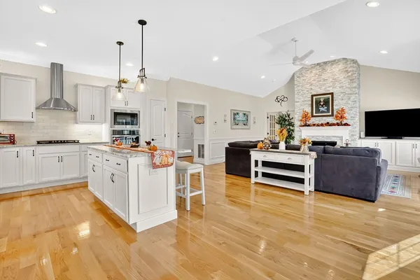 a large white kitchen with stainless steel appliances granite countertop a stove and a fireplace with wooden floor