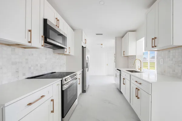 a kitchen with stainless steel appliances granite countertop white cabinets a sink a stove a microwave and a refrigerator