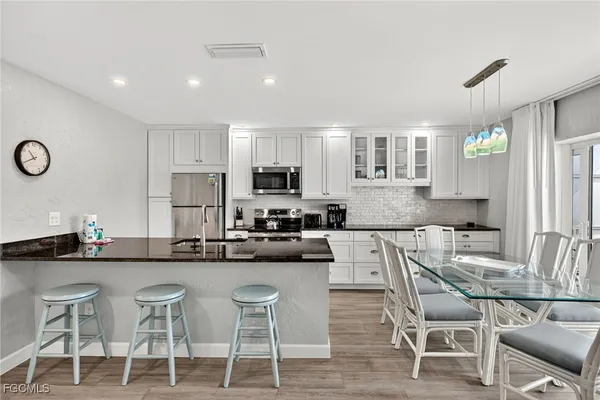 a kitchen with stainless steel appliances kitchen island granite countertop a dining table chairs and a refrigerator