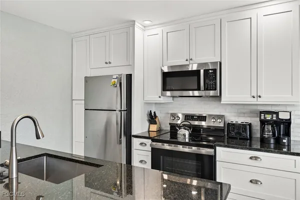 a kitchen with stainless steel appliances granite countertop a refrigerator a stove a sink and white cabinets