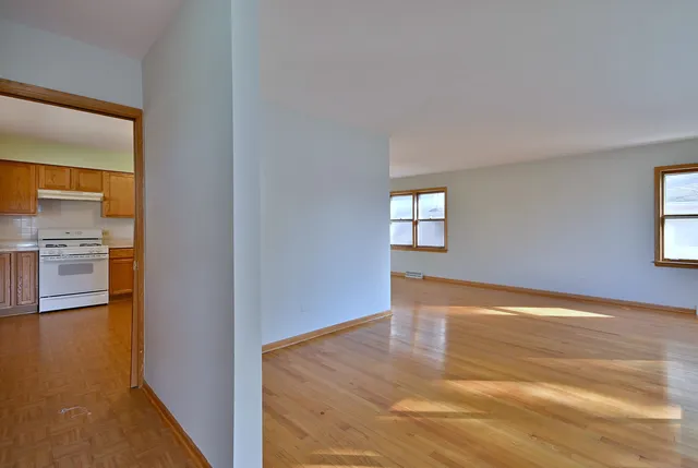 a view of empty room with wooden floor and kitchen view