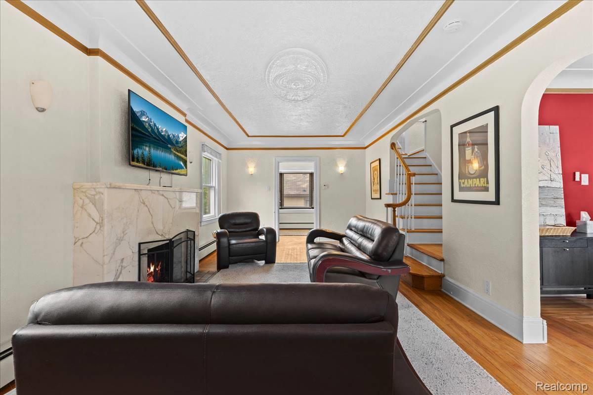 Living room featuring a marble fireplace, hardwood flooring, decorative ceiling molding, and a staircase with wood treads and white risers