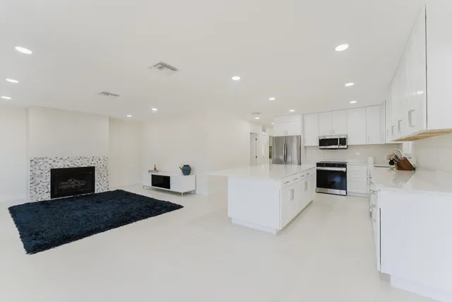 a large white kitchen with kitchen island a sink a center island and stainless steel appliances