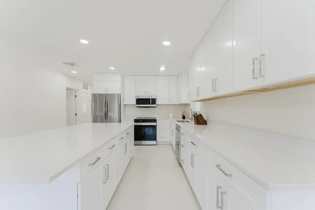 a large white kitchen with stainless steel appliances kitchen island a sink a stove a refrigerator and white cabinets