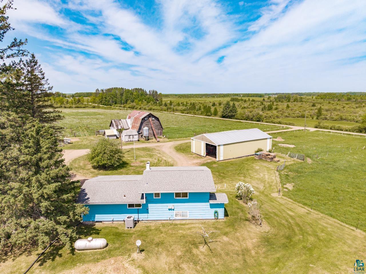 6606 Metso Road Kettle River, MN 55757 - Photo 3 of 84 Expansive rural property featuring a light blue residence with a gray roof, a large yellow outbuilding with a metal roof, and an aged barn with a red roof