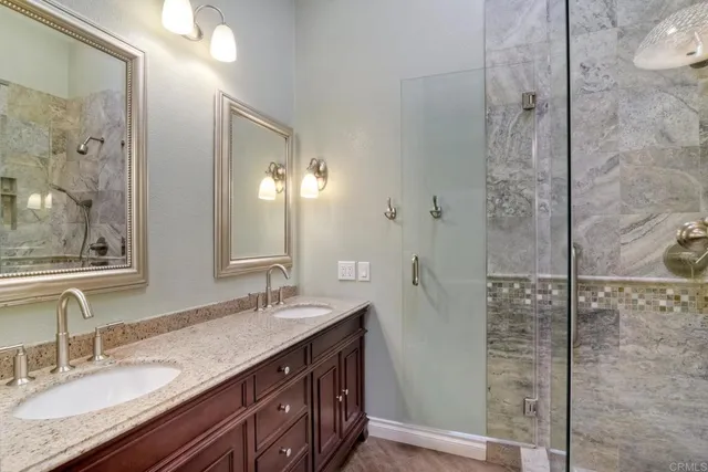 a bathroom with a granite countertop double vanity sink mirror and shower