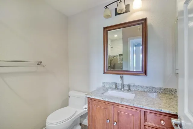 a bathroom with a granite countertop toilet a sink and mirror