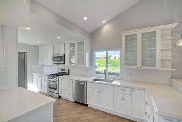 a kitchen with stainless steel appliances granite countertop a stove a sink dishwasher a refrigerator and white cabinets with wooden floor