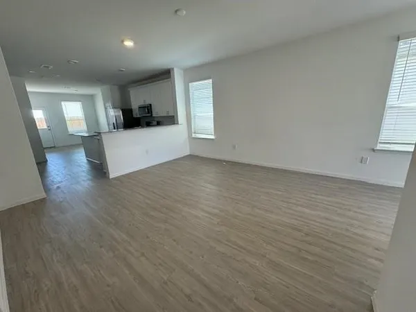 an empty room with wooden floor and a kitchen