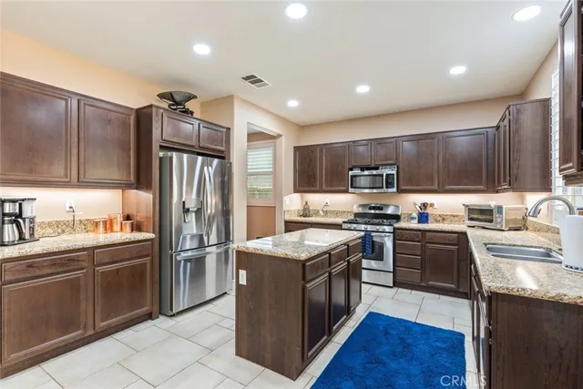 a kitchen with granite countertop stainless steel appliances a sink dishwasher a stove top oven a refrigerator with grey cabinets and wooden floor