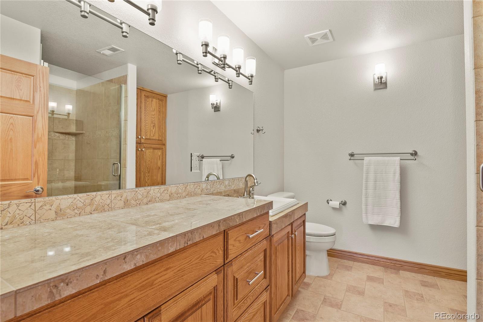 5220 Roundup Ridge Road Colorado Springs, CO 80908 - Photo 30 of 50 a spacious bathroom with a granite countertop sink a toilet a mirror and shower