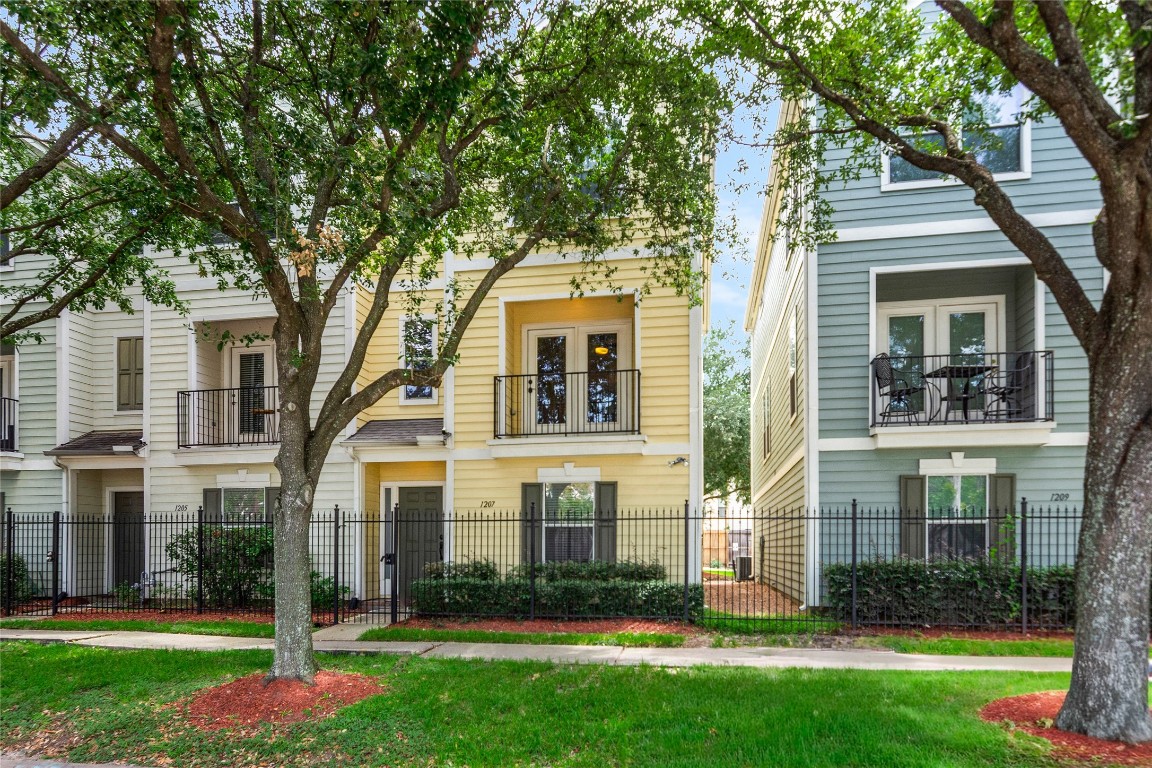 Charming end unit townhouse with a modern exterior, featuring a fenced front yard and balcony.  Mature trees and well-maintained landscaping enhance its curb appeal.