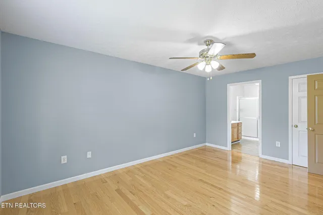 a view of an empty room with chandelier fan and wooden floor