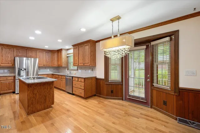 a kitchen with stainless steel appliances granite countertop a refrigerator a sink dishwasher a stove and a dining table with wooden cabinet