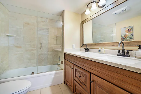 a bathroom with a granite countertop sink a toilet a mirror a bathtub and shower