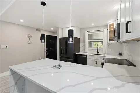 a large white kitchen with a sink a refrigerator and chairs