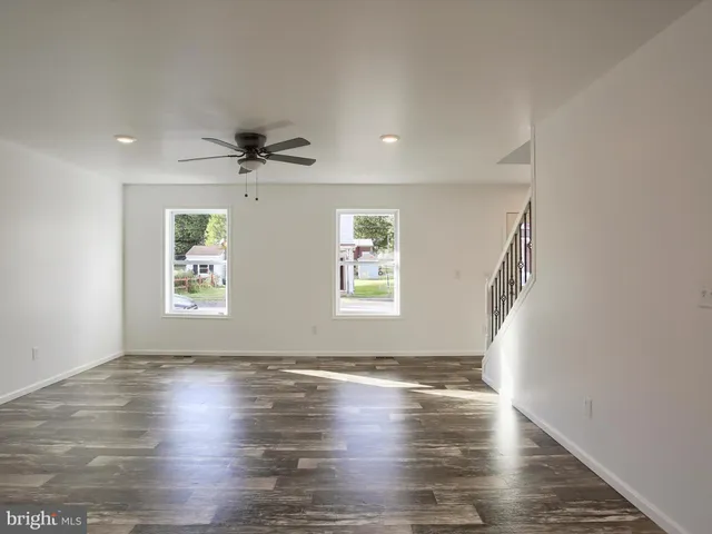 an empty room with wooden floor chandelier fan and windows