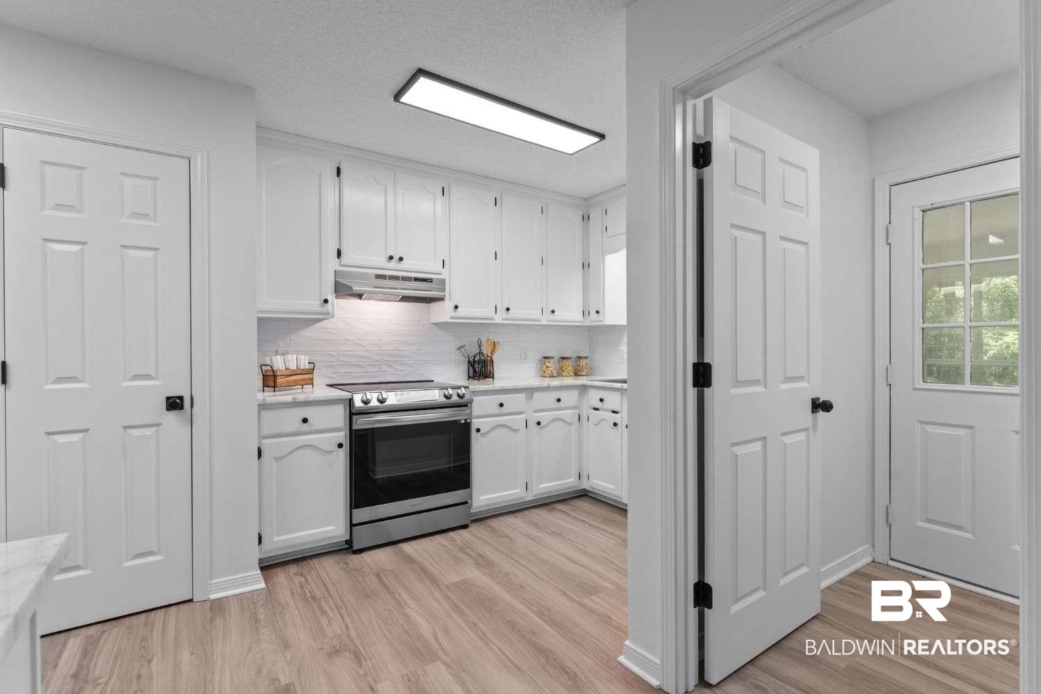 10251 Windmill Road Fairhope, AL 36532 - Photo 22 of 44 Kitchen with stainless steel range with electric cooktop, under cabinet range hood, white cabinets, light wood finished floors, and light countertops