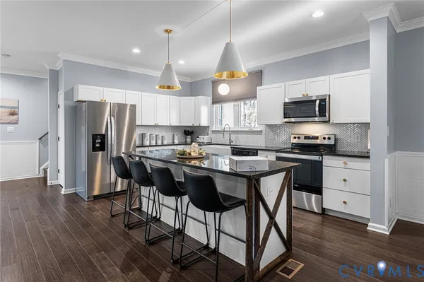 a kitchen with stainless steel appliances kitchen island granite countertop a refrigerator a stove a microwave oven a sink with island and chairs with wooden floor