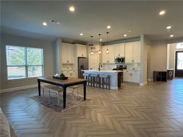 a room with stainless steel appliances kitchen island granite countertop a table chairs sink and cabinets