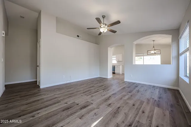 a view of an empty room with wooden floor and a ceiling fan