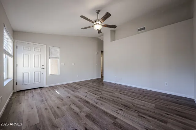 an empty room with wooden floor fan and windows