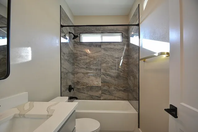 a bathroom with a granite countertop bathtub shower sink vanity and toilet