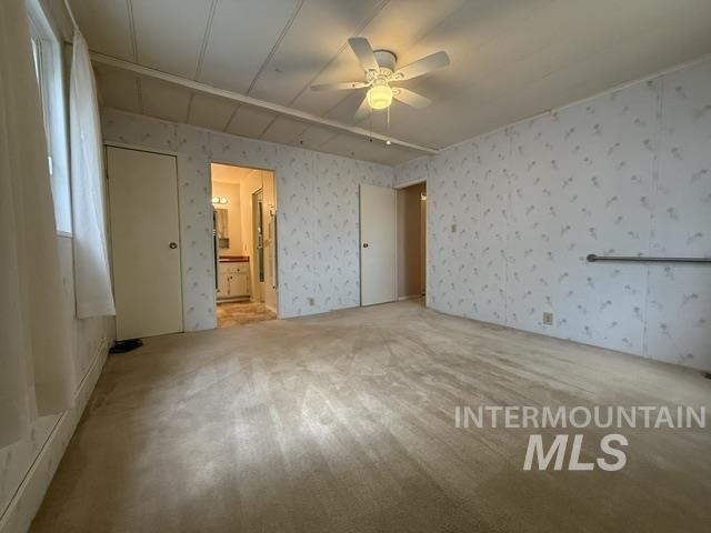 1360 Pioneer Road Weiser, ID 83672 - Photo 11 of 47 Spacious room featuring neutral carpeting, patterned wallpaper, a ceiling fan with integrated lighting, and white paneled doors