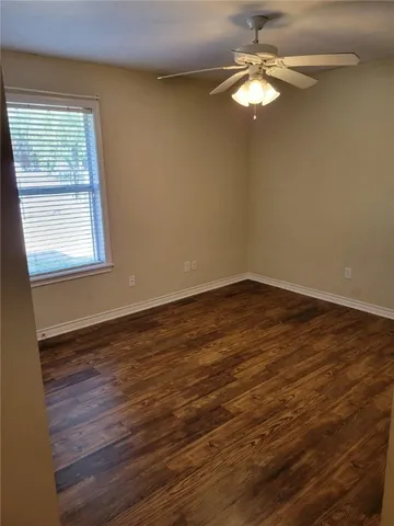 an empty room with wooden floor chandelier fan and windows