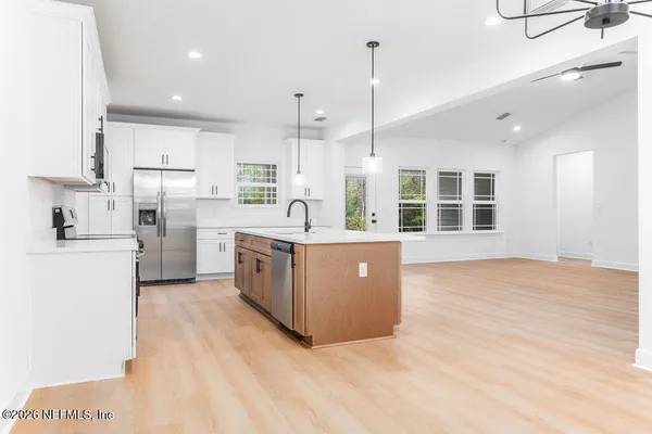 a kitchen with stainless steel appliances granite countertop a stove a sink a refrigerator and white cabinets with wooden floor