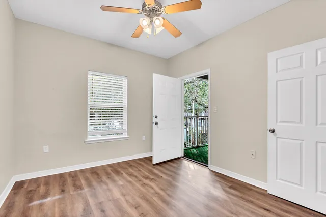an empty room with wooden floor chandelier fan and windows