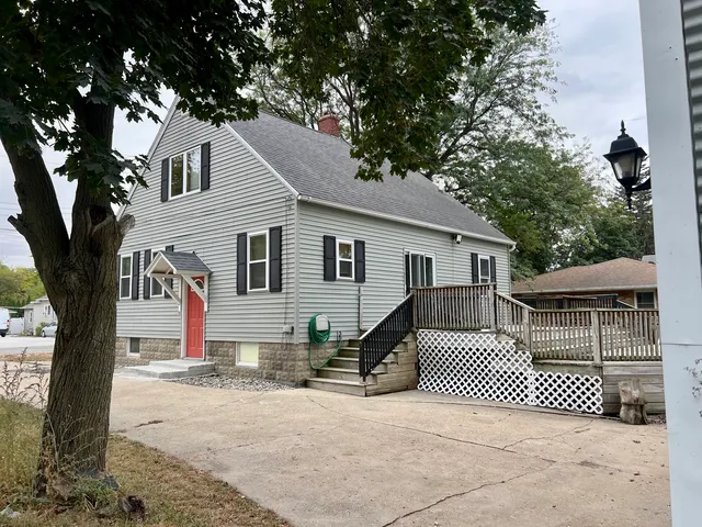 a view of a white house with a large tree and wooden fence