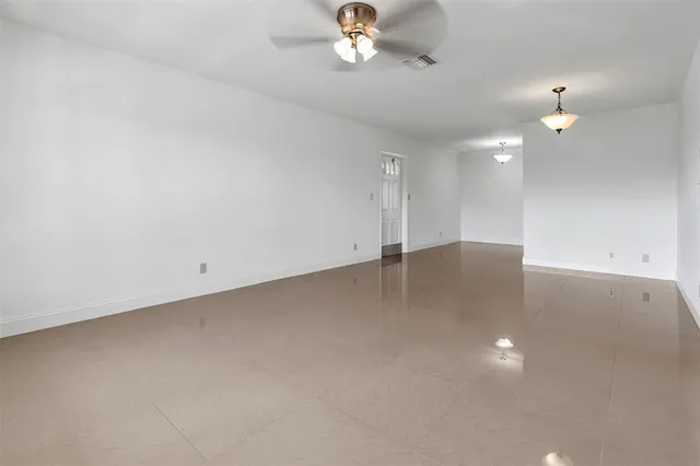 an empty room with a chandelier fan and wooden floor
