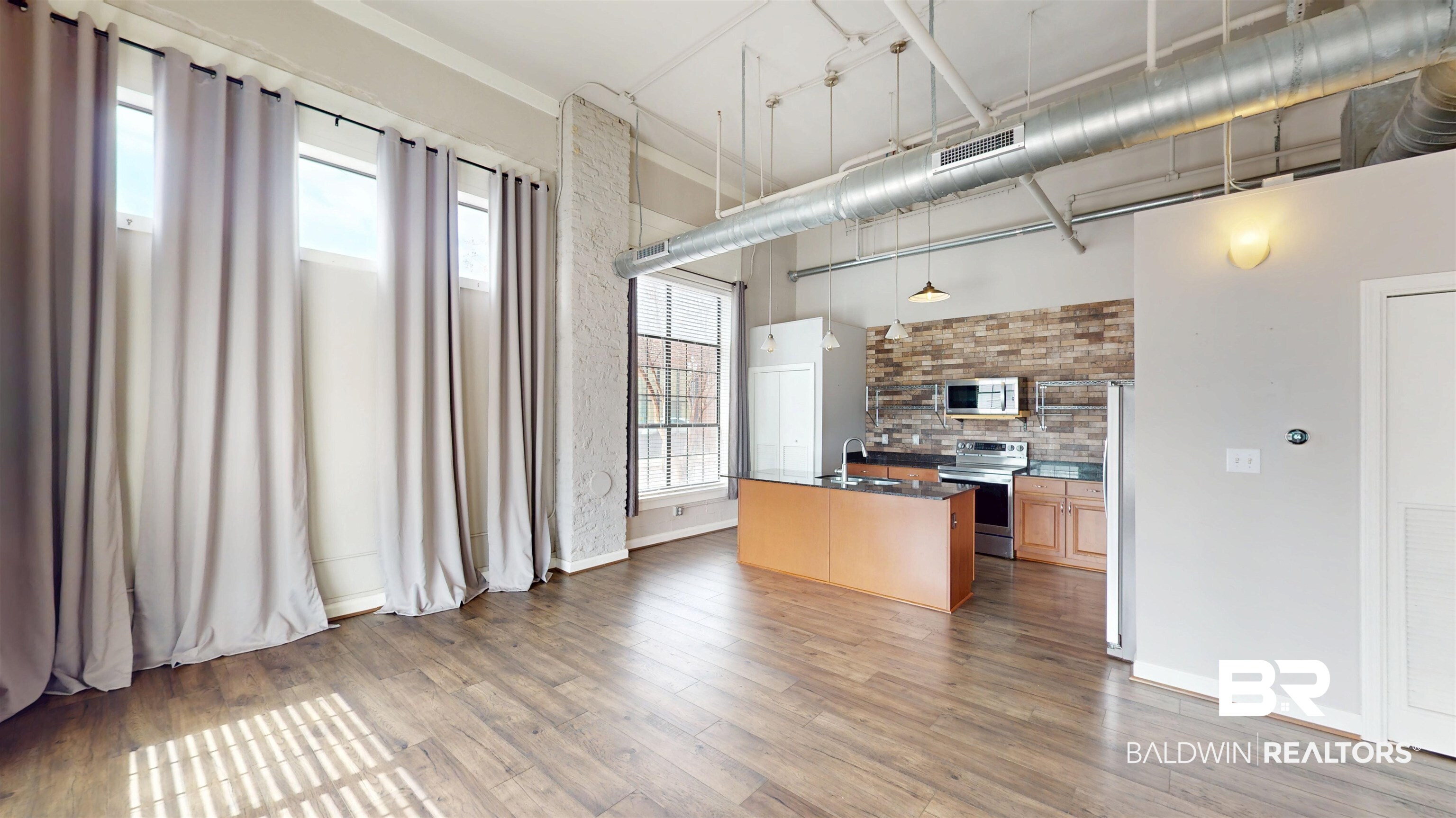 308 St Louis Street, Unit 101 Mobile, AL 36602 - Photo 27 of 30 Kitchen featuring an island with sink, stainless steel appliances, pendant lighting, light wood-style flooring, and a high ceiling