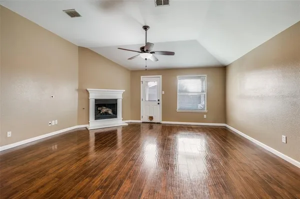a view of an empty room with wooden floor fireplace and a window