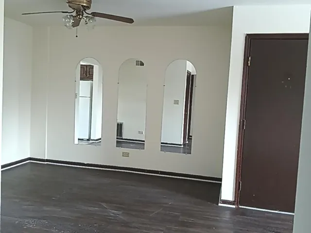 an empty room with wooden floor mirror and windows