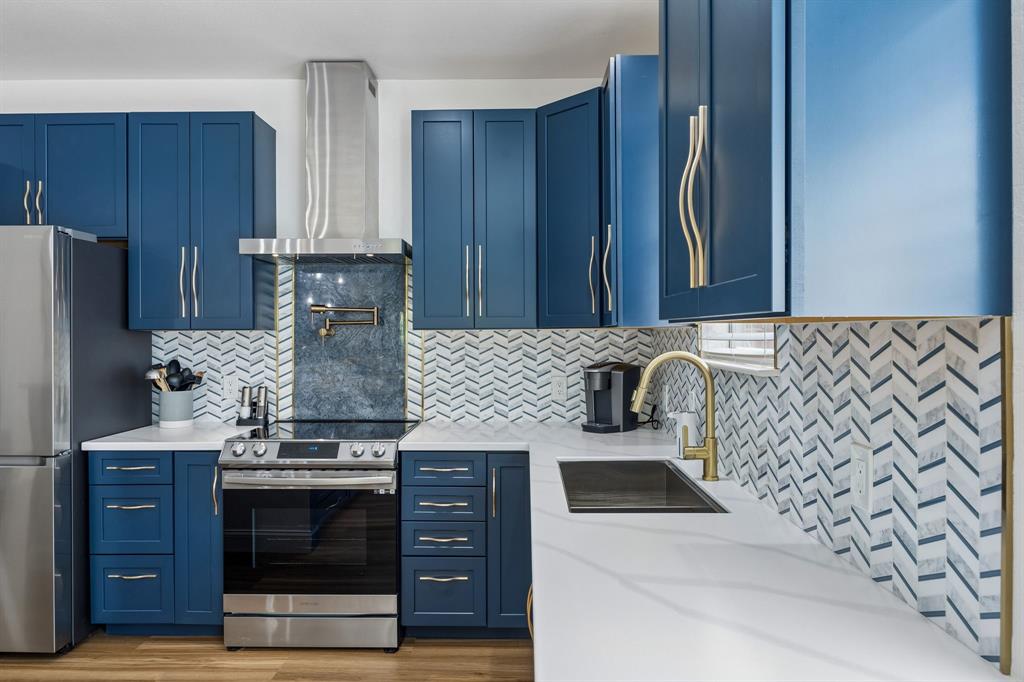 9217 Inverness Drive Rowlett, TX 75089 - Photo 8 of 40 Stylish Kitchen Focal Point — Navy cabinetry, brushed gold hardware, quartz counters, a stainless vent hood, and a pot filler give this kitchen a bold, modern look with practical function.