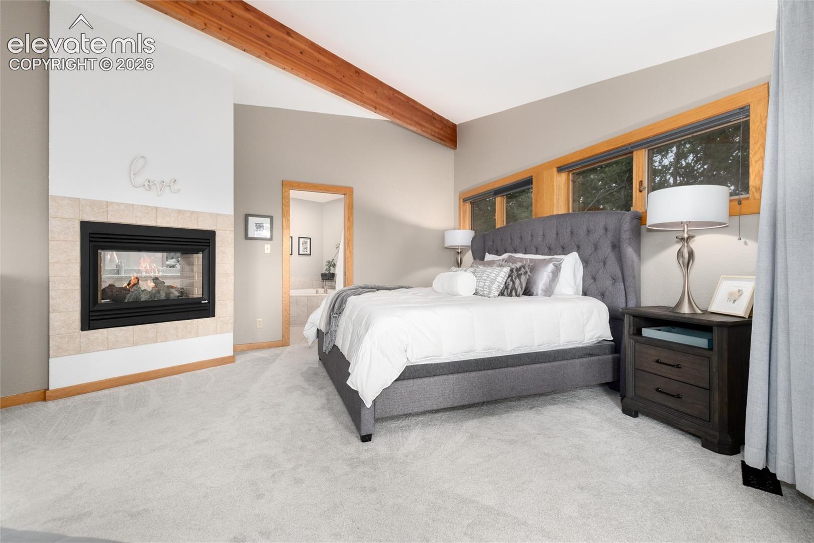 12730 Bridle Bit Road Colorado Springs, CO 80908 - Photo 14 of 48 Room featuring a gas fireplace with a tiled surround, exposed wood beams, and warm wood-framed windows