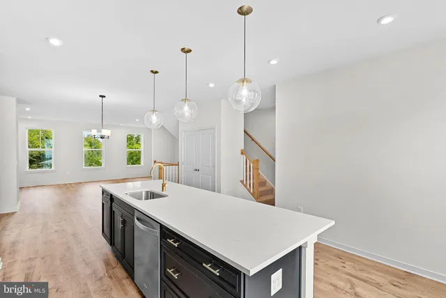 a large white kitchen with a sink a center island a stove wooden floor and staircase