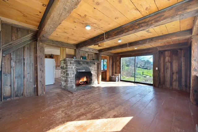 a view of an empty room with wooden floor fireplace and a window