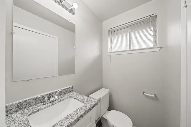 a bathroom with a granite countertop sink toilet and mirror