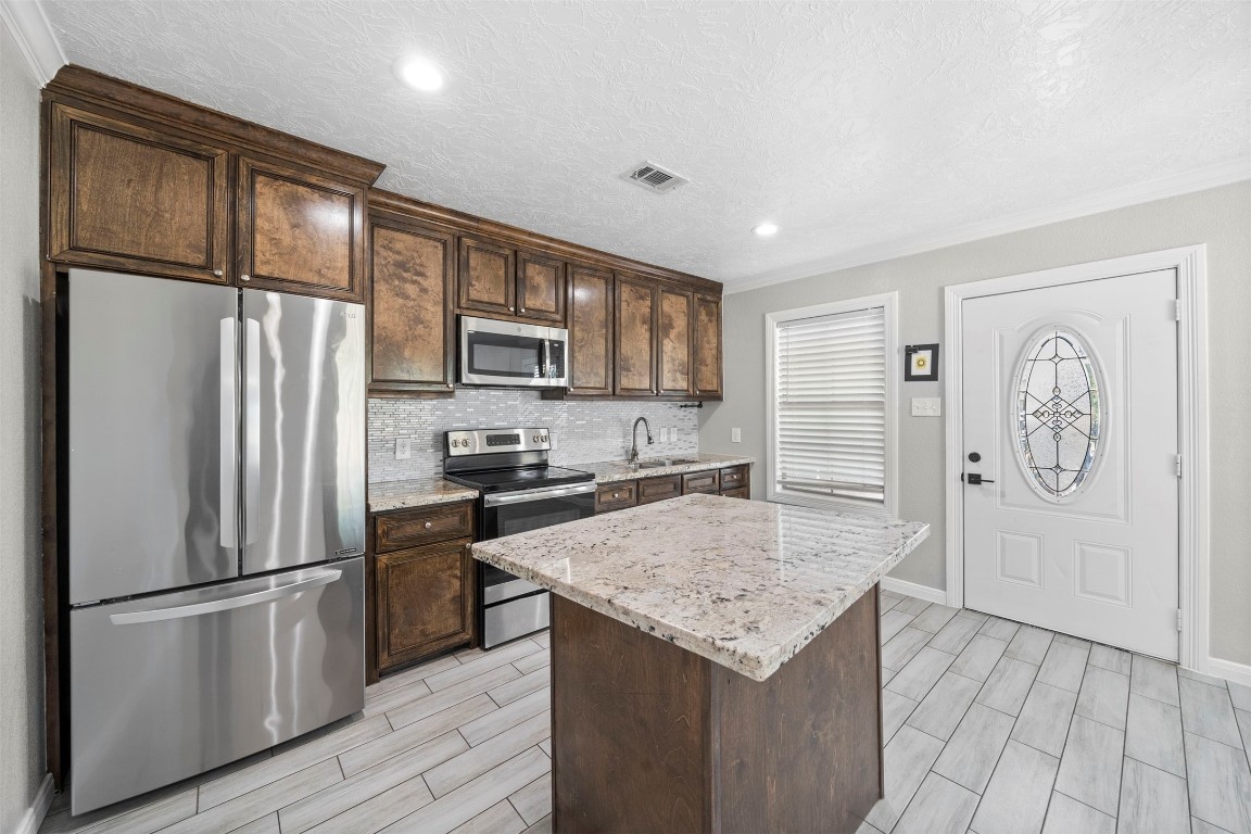 7941 Goode Street Houston, TX 77012 - Photo 22 of 26 a kitchen with granite countertop stainless steel appliances a refrigerator a stove top oven and wooden floors