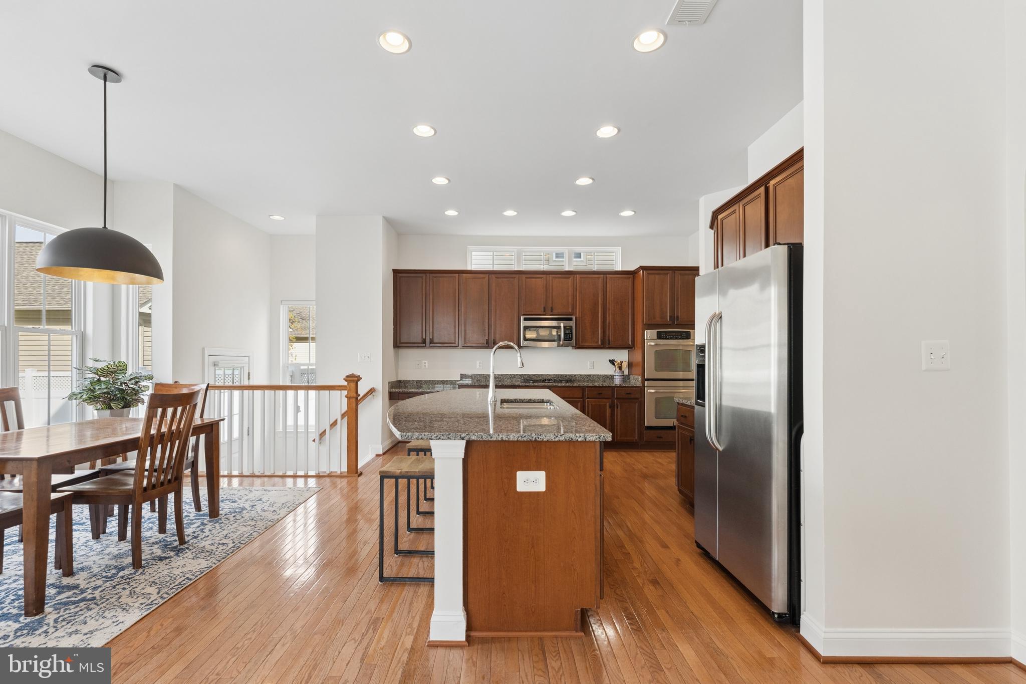 23342 Higbee Lane Brambleton, VA 20148 - Photo 26 of 73 a kitchen with stainless steel appliances granite countertop a refrigerator a stove a sink dishwasher a dining table and chairs with wooden floor