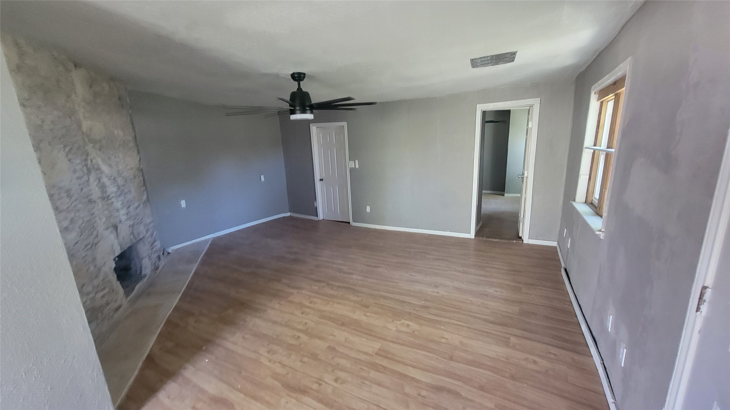 12018 Sandpiper Road Angleton, TX 77515 - Photo 39 of 48 This room features laminate wood flooring, a stone accent wall, and a ceiling fan. It has a neutral color scheme and ample natural light from the window. There’s a doorway leading to another room, adding to the open feel.