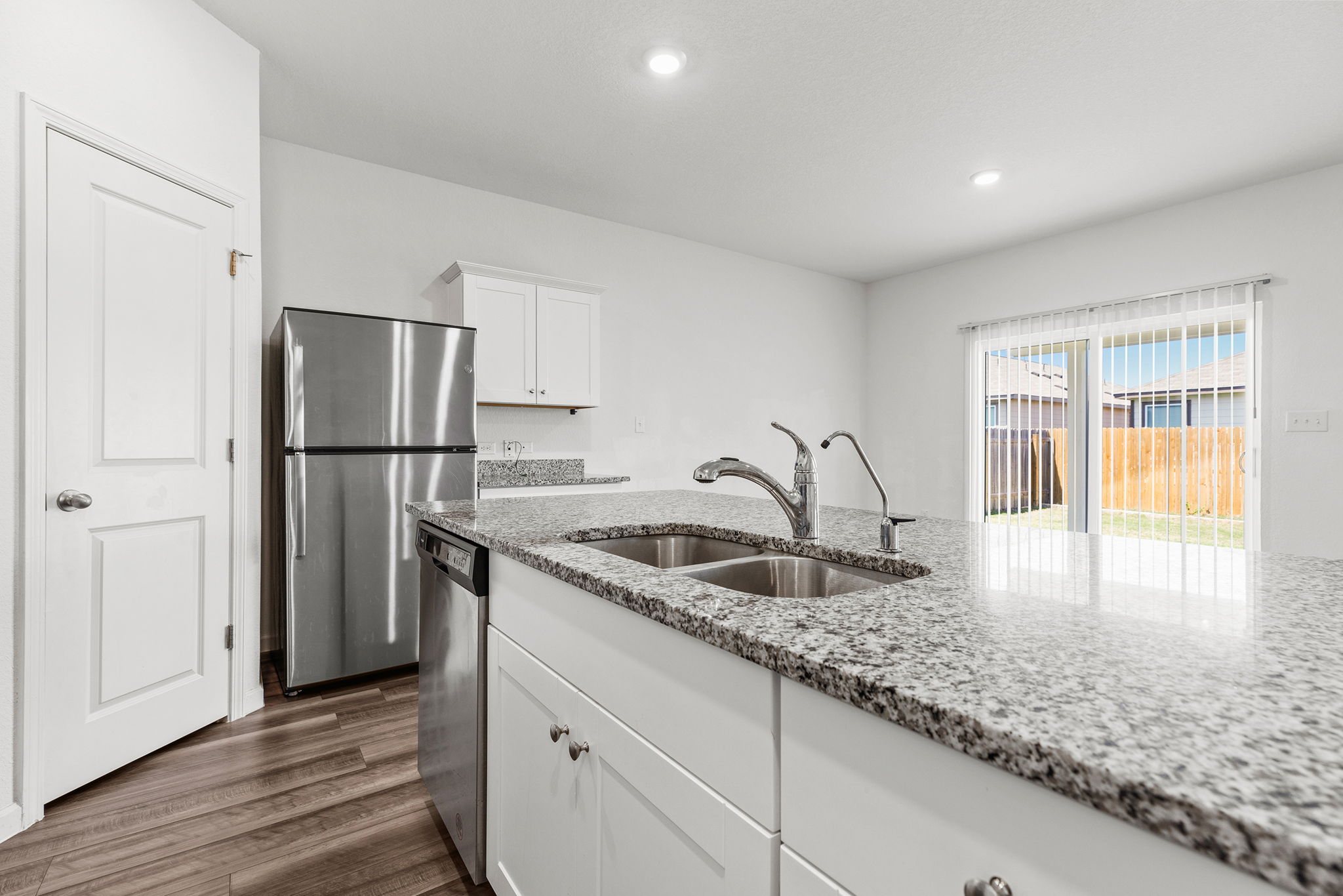 409 Line Of Fire Way Jarrell, TX 76537 - Photo 7 of 30 Kitchen featuring granite countertops, stainless steel appliances, white cabinetry, center island with sink, wood-finish flooring, recessed lighting, and adjoining dining area.