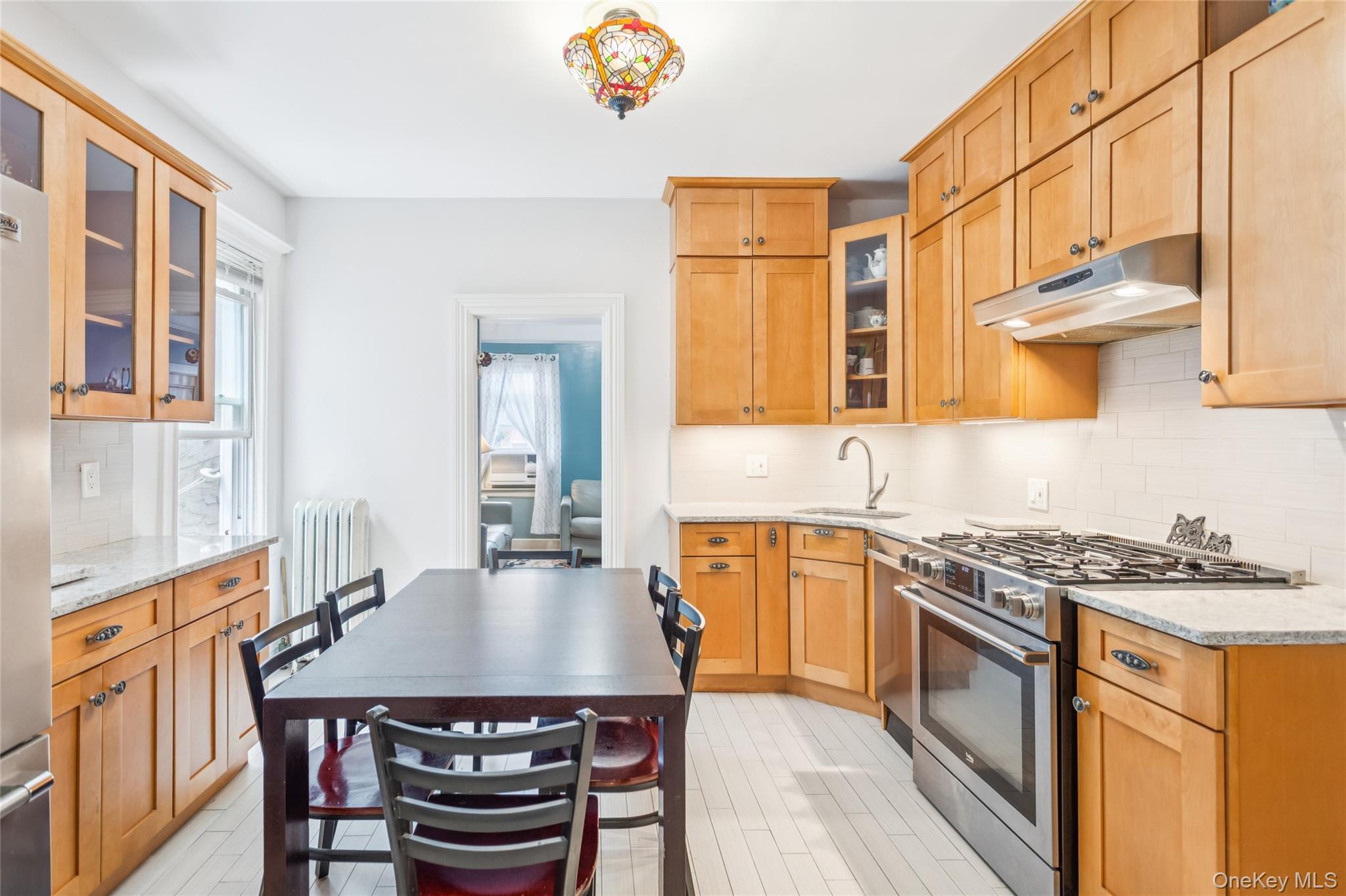 45-09 104th Street Queens, NY 11368 - Photo 2 of 21 Kitchen with stainless steel range with gas cooktop, under cabinet range hood, radiator heating unit, tasteful backsplash, and light stone countertops