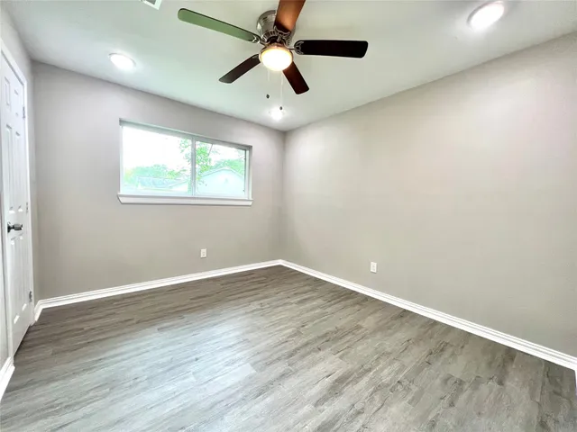 an empty room with wooden floor ceiling fan and windows